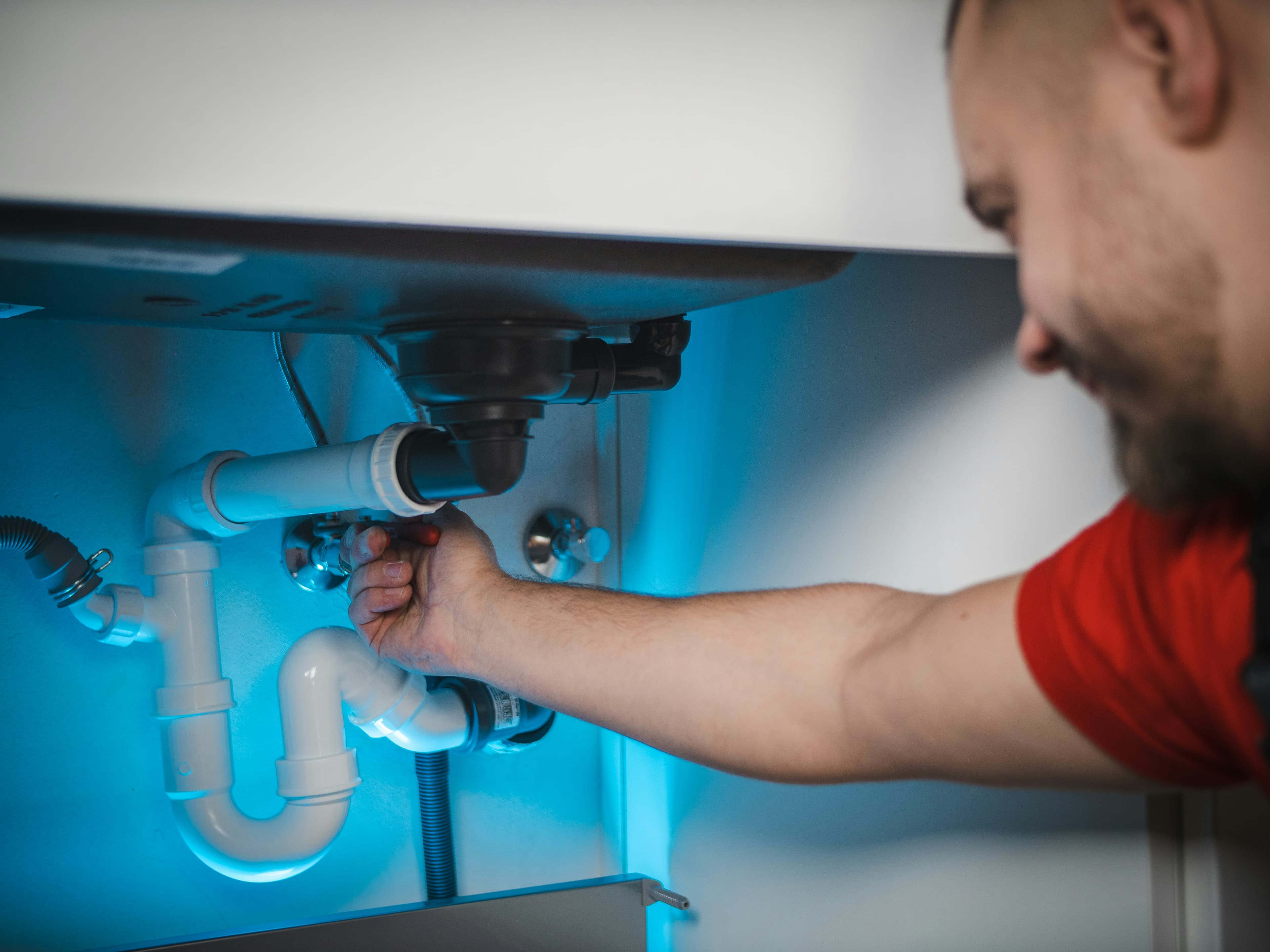 Plumber repairing pipework beneath a sink